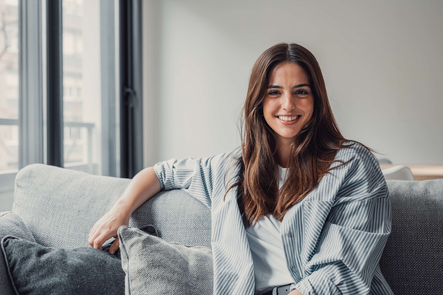 smiling woman in a blue shirt sitting on a sofa